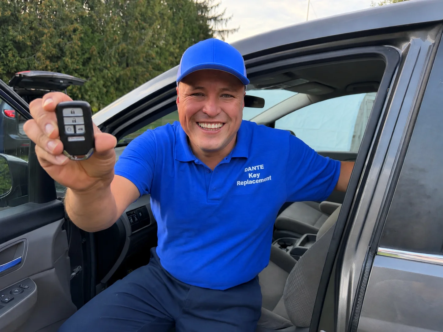 Dante of Dante Key Replacement, in a branded work shirt, holding up a smart key fob from the doorway of a vehicle.