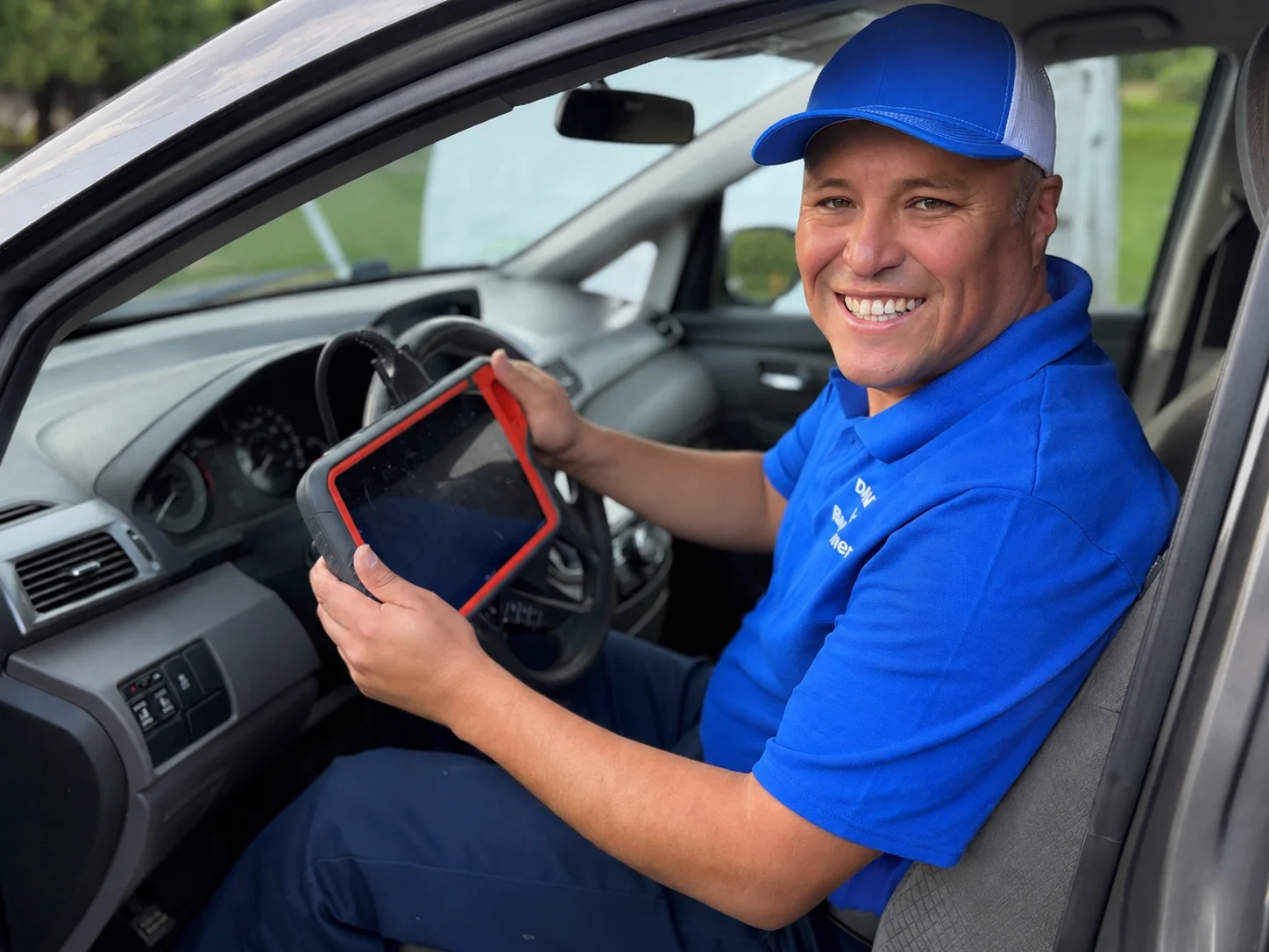 Dante in the driver seat of a vehicle, holding a key programming tablet connected to the vehicle.