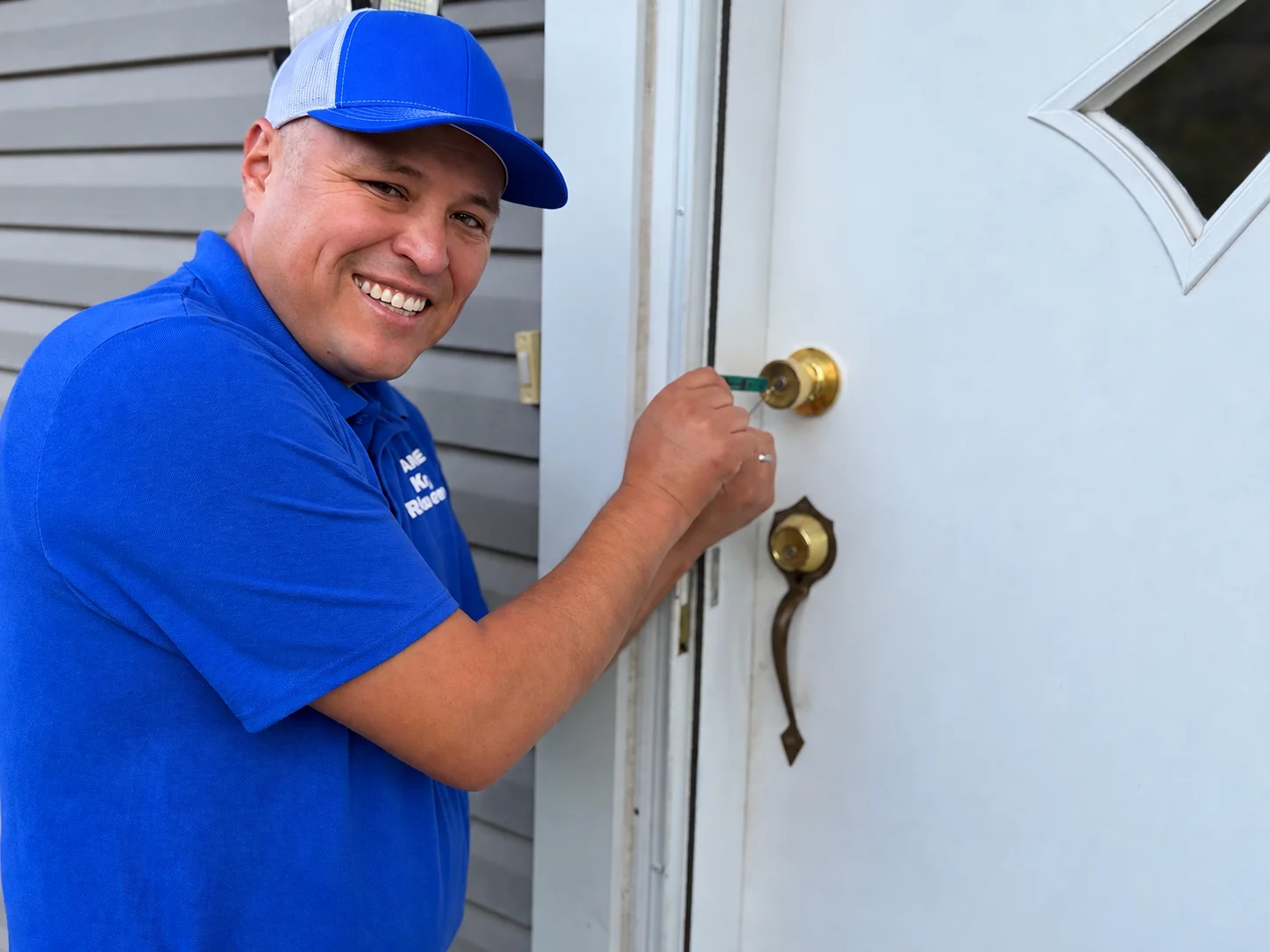 Dante picking the knob lock on a residential front door, in a branded work shirt.