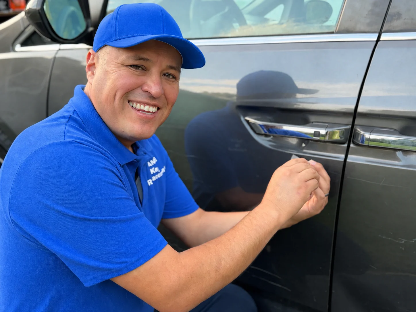 Dante smiling at the camera while working at a vehicle door with a slim entry tool.